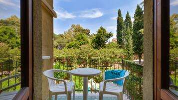 Un balcón con mesa y sillas, un bolso azul, y vistas a un jardín con árboles y un parque infantil.