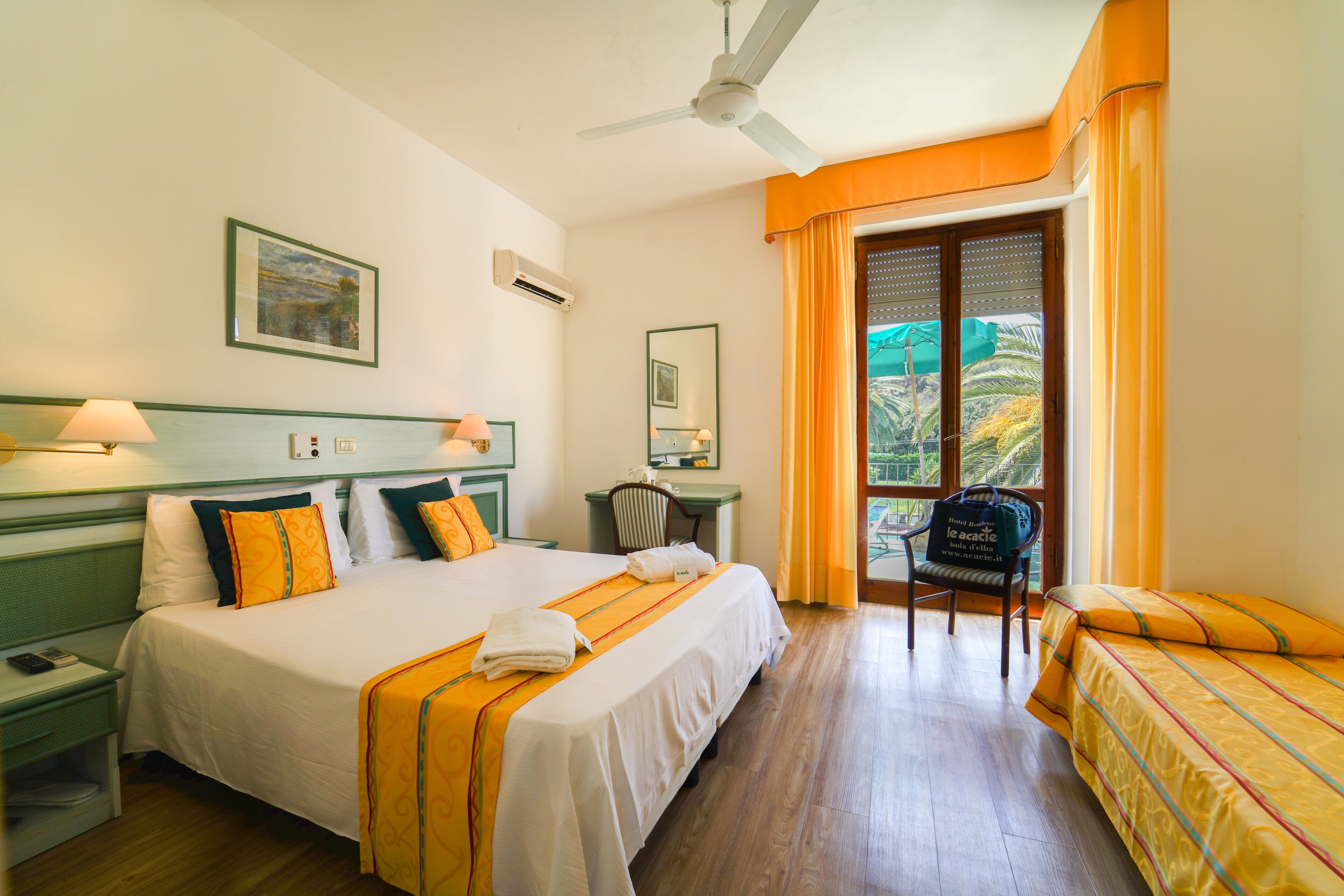 Una camera d'hotel con un letto, una scrivania, una sedia e un balcone con tende.