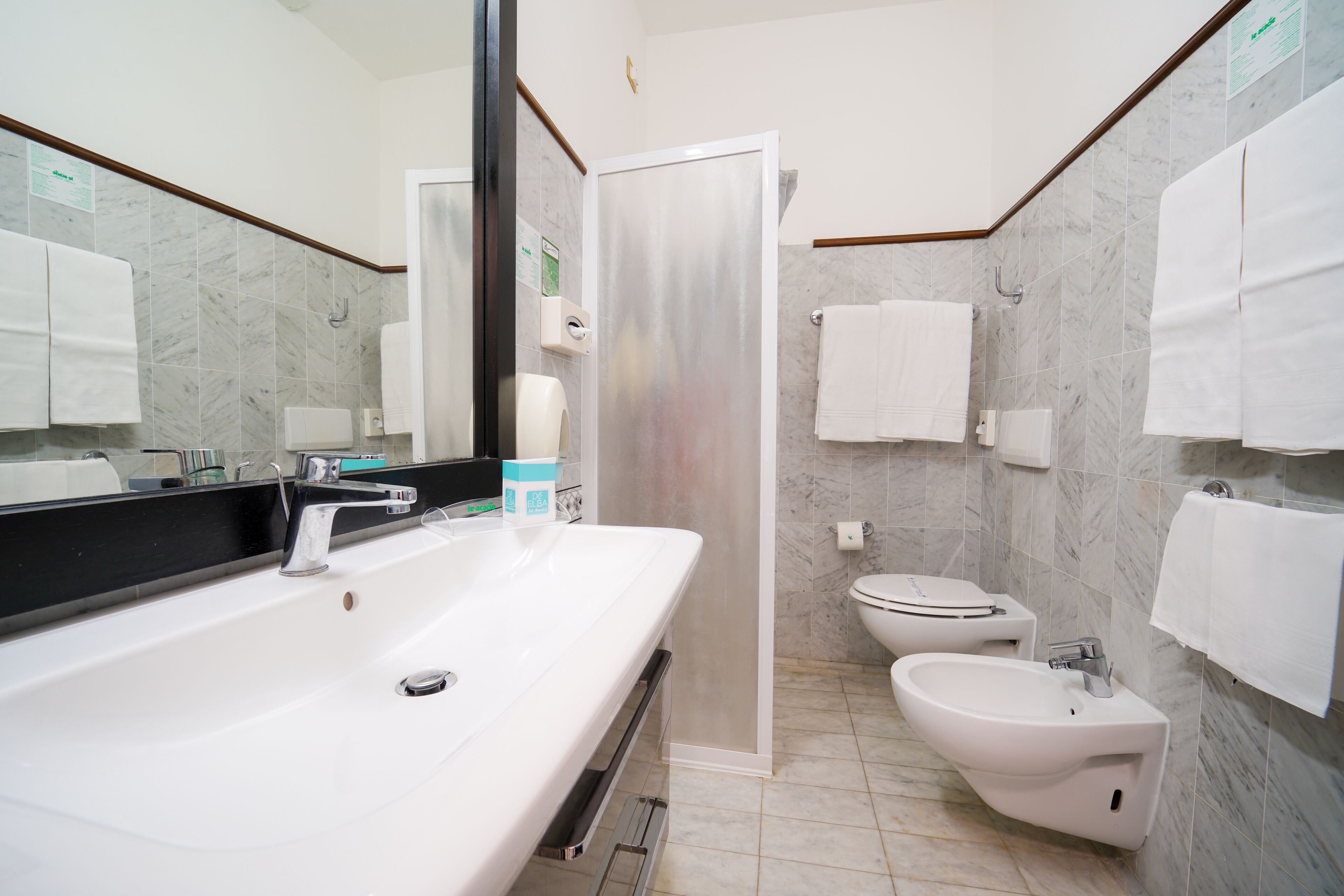 A modern bathroom with a large mirror, a white sink, a bidet, and a toilet.
