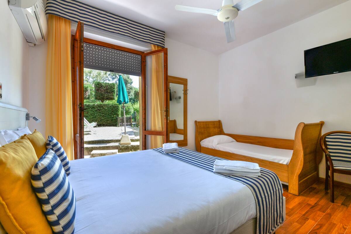 A hotel room with a large bed, a smaller bed, a chair, a TV, and a window with curtains.