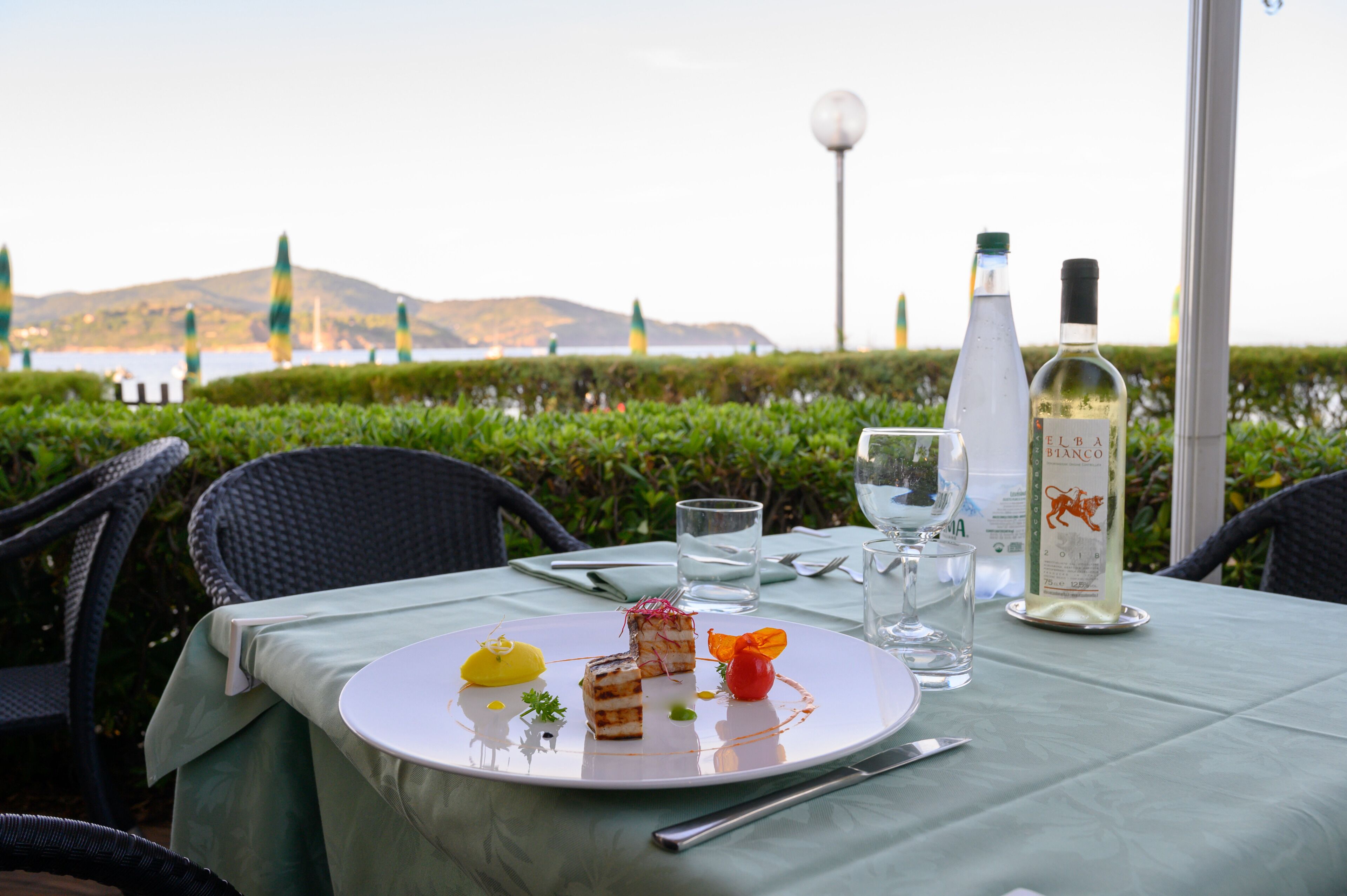 A table set for a meal with a bottle of white wine, a glass of water, and a plate with food.