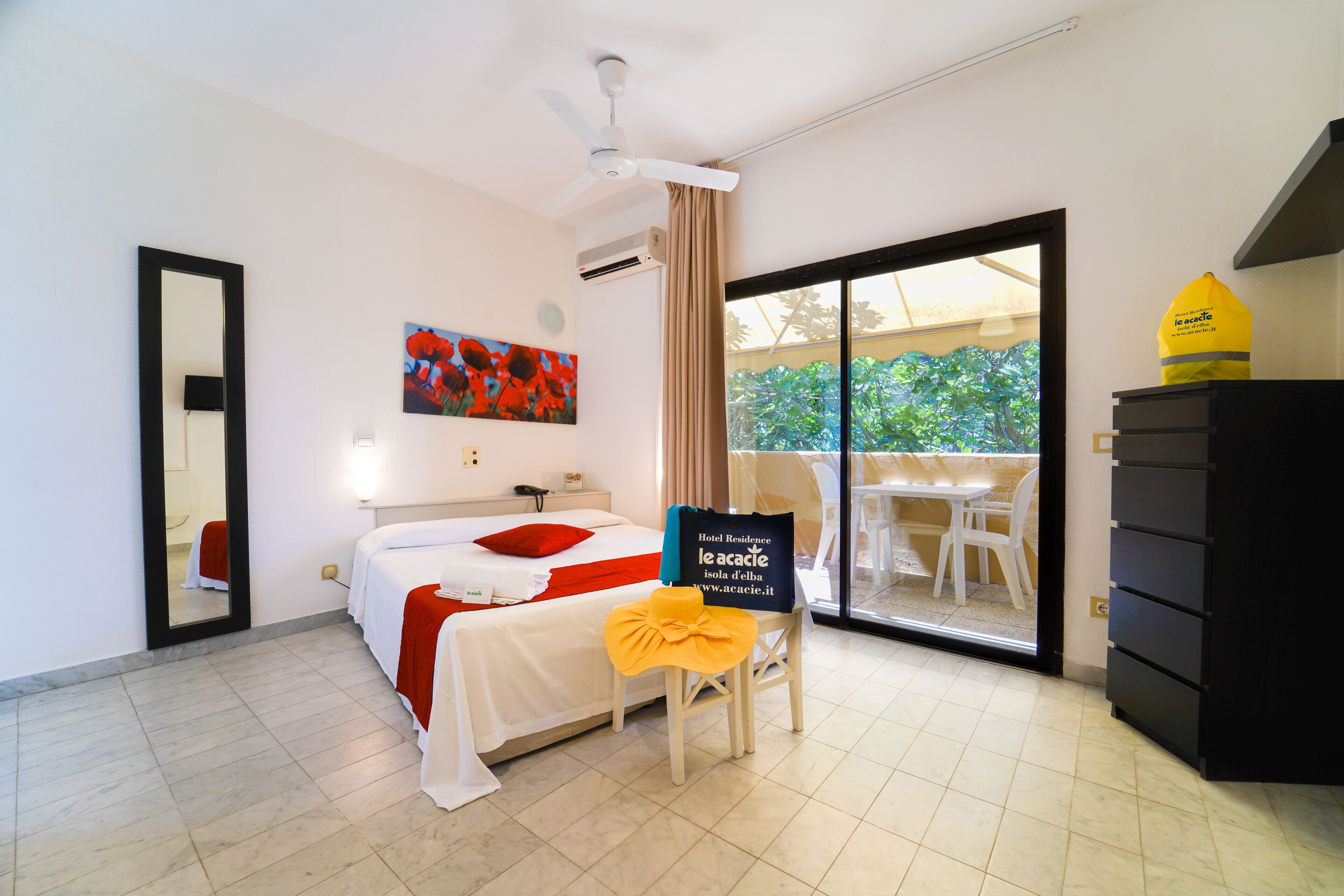 A hotel room with a bed, a chair with a towel, a desk, a mirror, and a view of the outdoors.