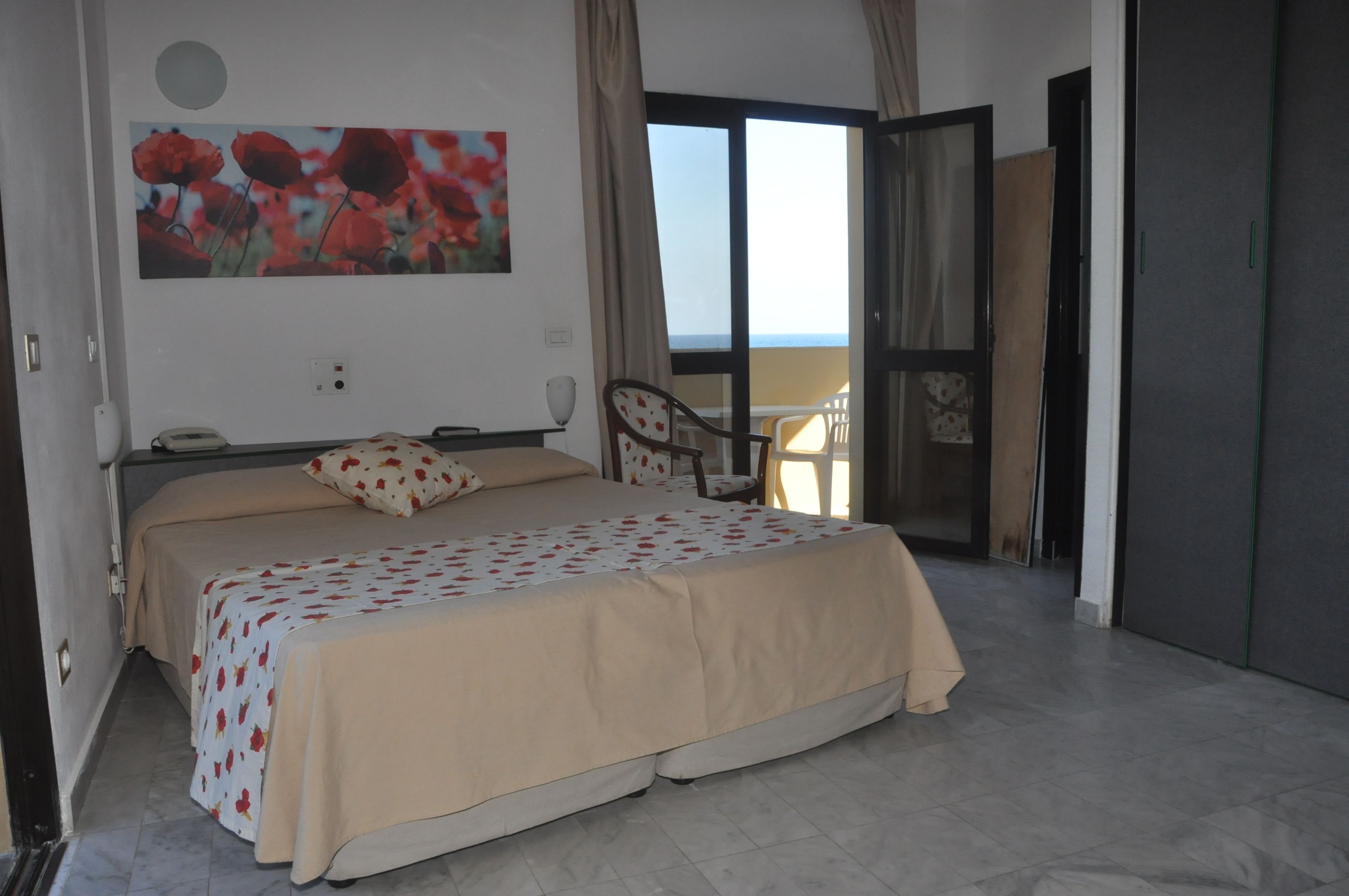 A bedroom with a bed, a chair, a painting, and a view of the sea.