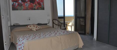 A bedroom with a bed, a chair, a painting, and a view of the sea.