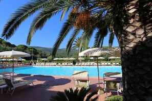 A poolside area with lounge chairs and umbrellas, surrounded by palm trees and a clear blue sky. - Hotel Le Acacie (Capoliveri)