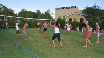 Un gruppo di persone gioca a pallavolo su un prato, con un albergo chiamato "HOTELLE ACACIE" sullo sfondo.