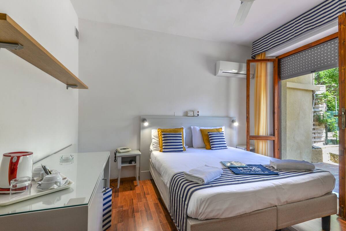 A hotel room with a bed, bedside table, and a window with a view of the outdoors.