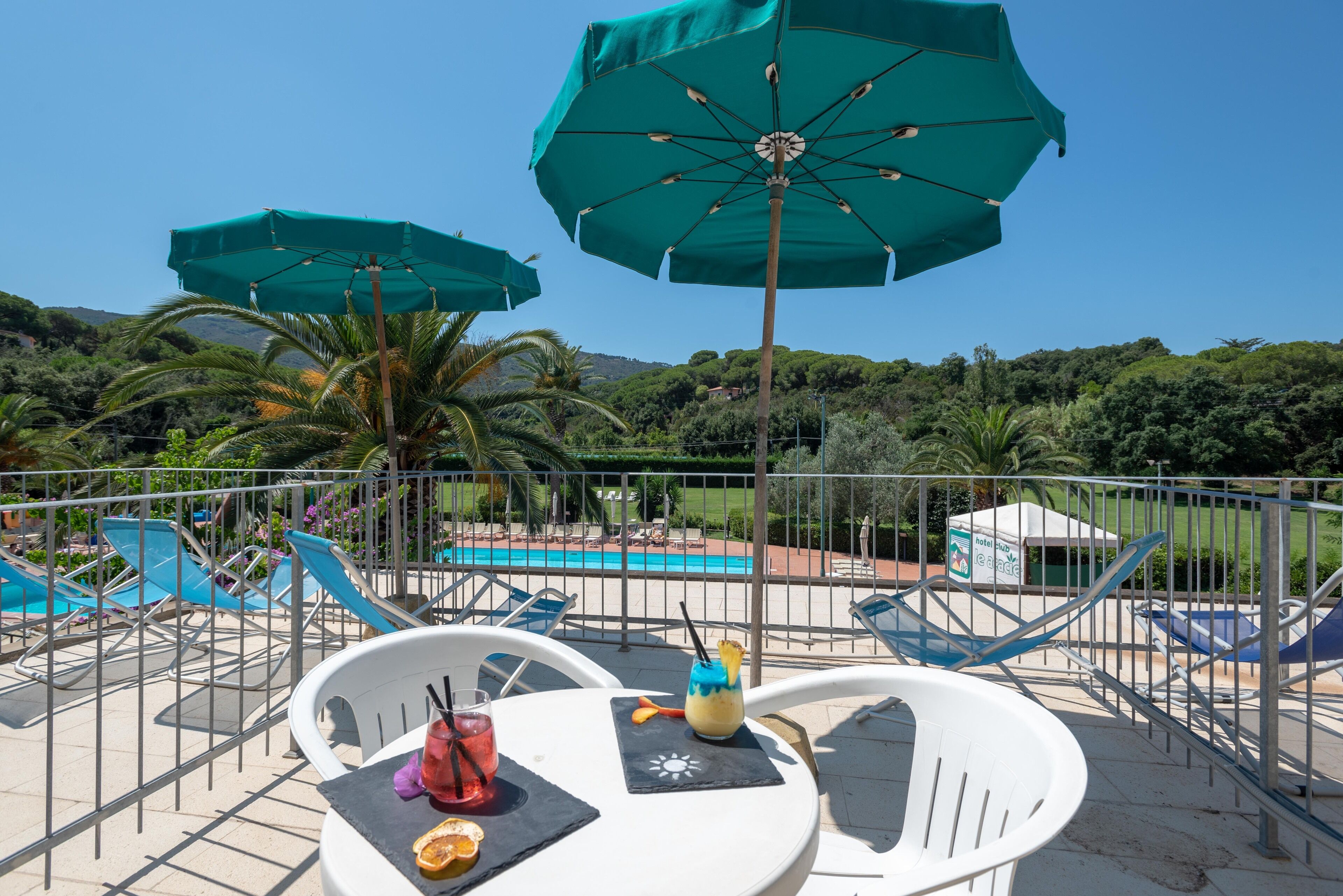 A poolside area with lounge chairs, umbrellas, and a table with drinks.