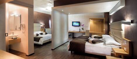 A modern hotel room with a large bed, a TV, a desk, and a bathroom with a mirror and sink.