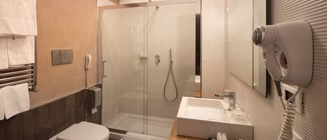 A modern bathroom with a glass-enclosed shower, a toilet, a sink, and a hairdryer mounted on the wall.