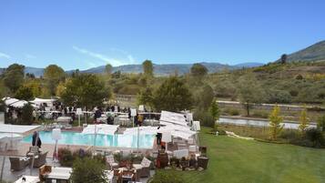 An outdoor pool area with lounge chairs and tables, surrounded by greenery and hills in the background.