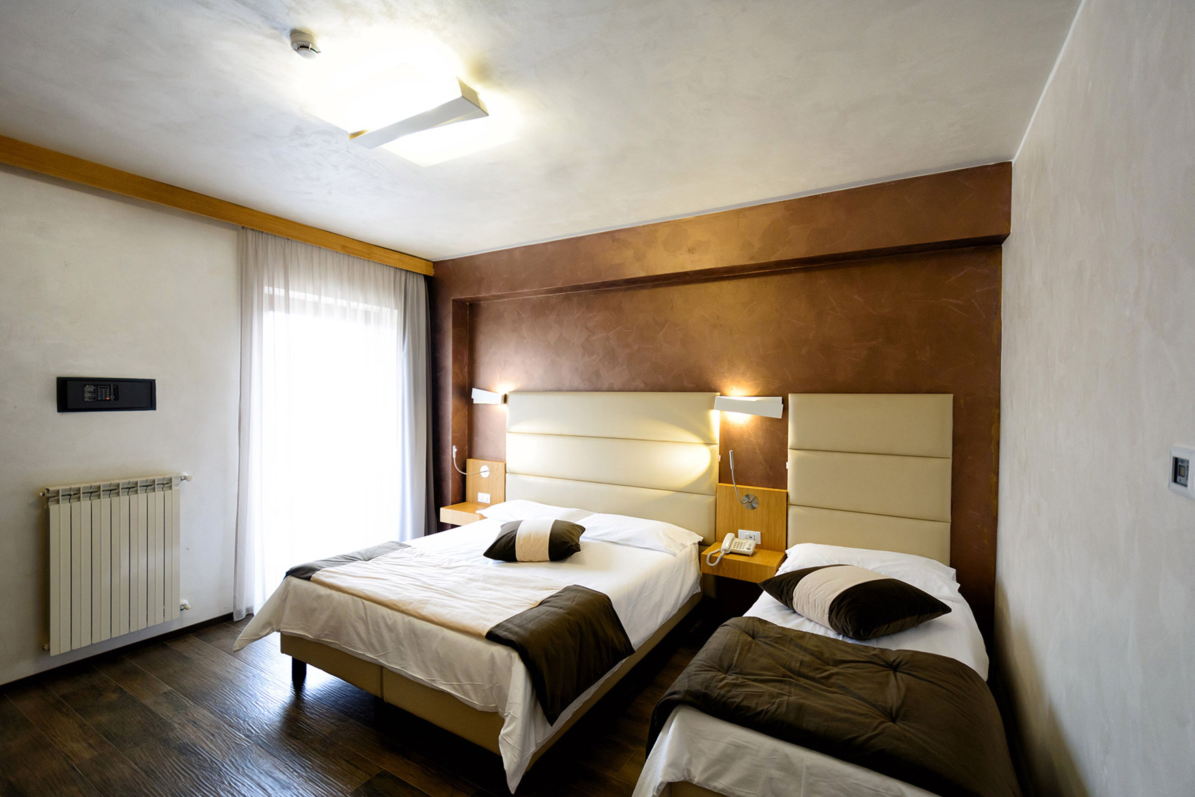 A hotel room with two beds, a radiator, a telephone, and a window with curtains.