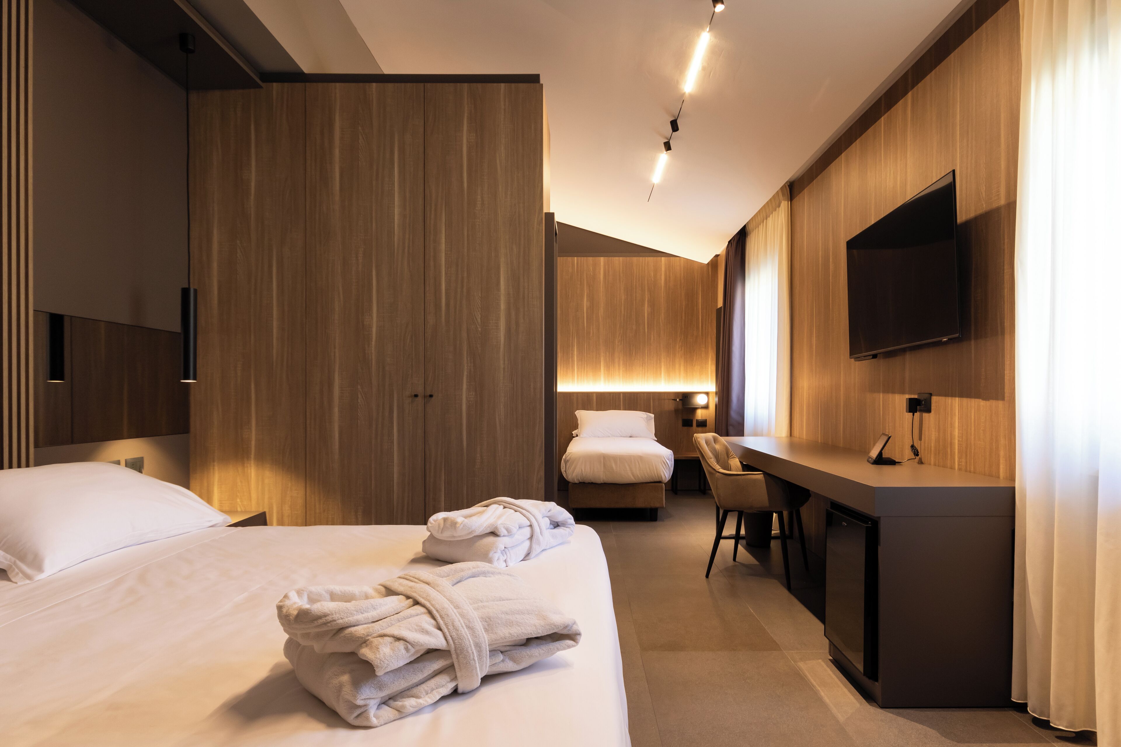 Una habitación de hotel moderna con una cama grande, un escritorio, una silla y un televisor fijado a la pared.