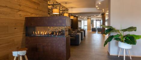 A modern lobby with a stone wall, a fireplace, seating area, and a large potted plant.