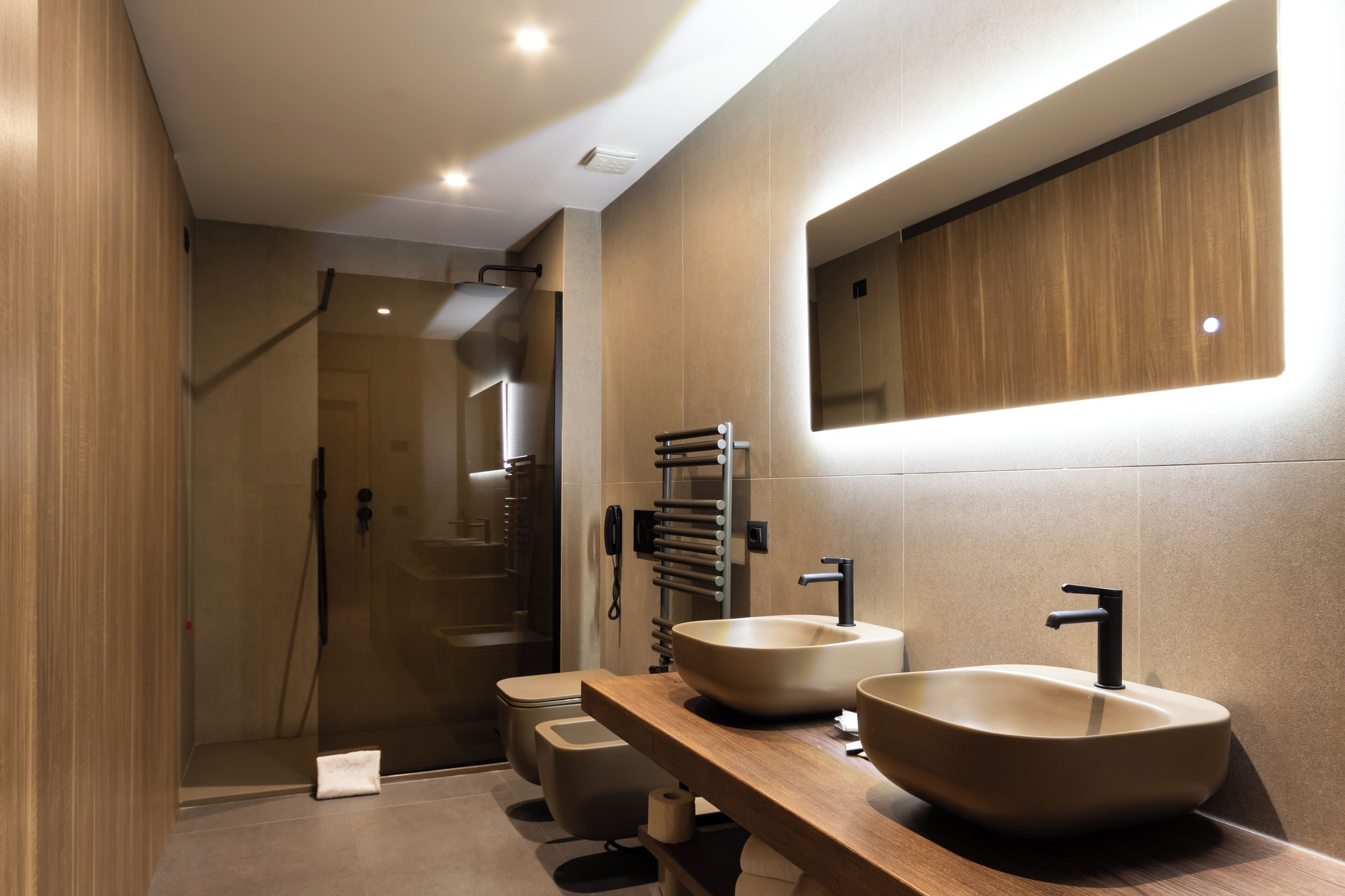 Un baño moderno con un espejo grande, dos lavamanos, una ducha y un inodoro.