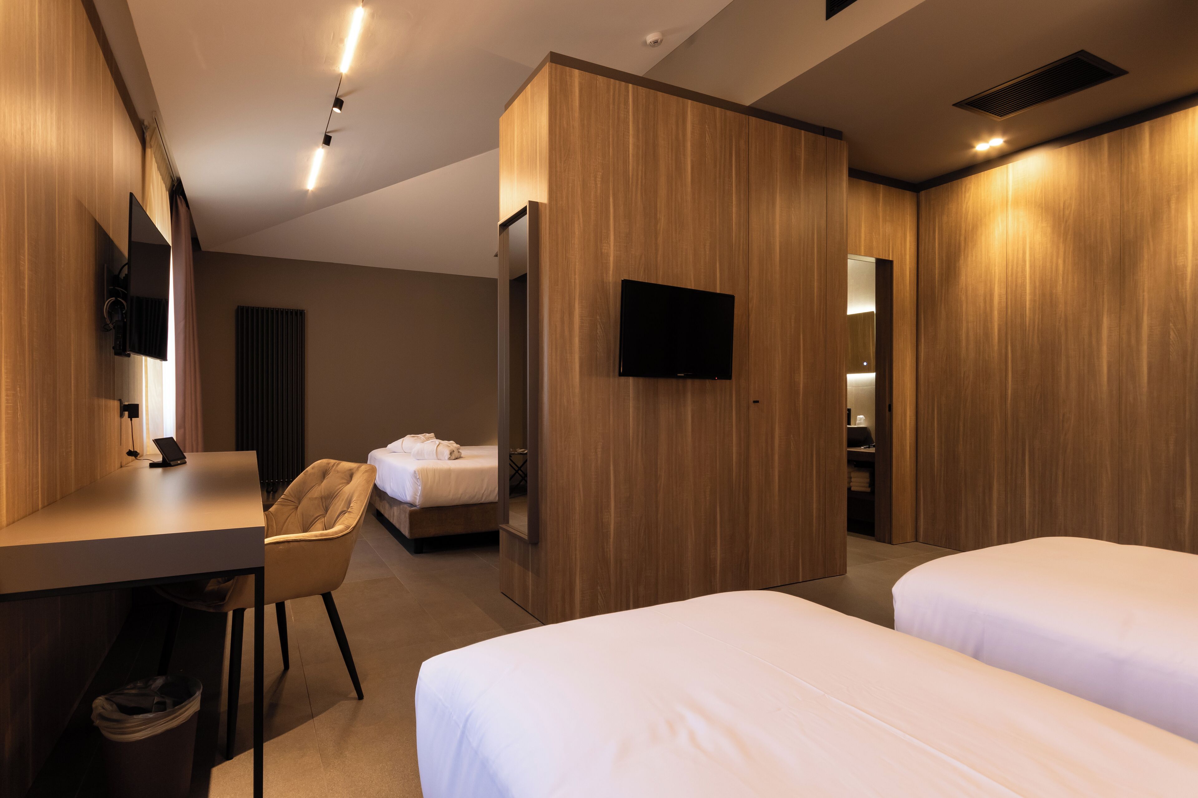 A modern hotel room with a desk, two beds, a TV, and a wardrobe.