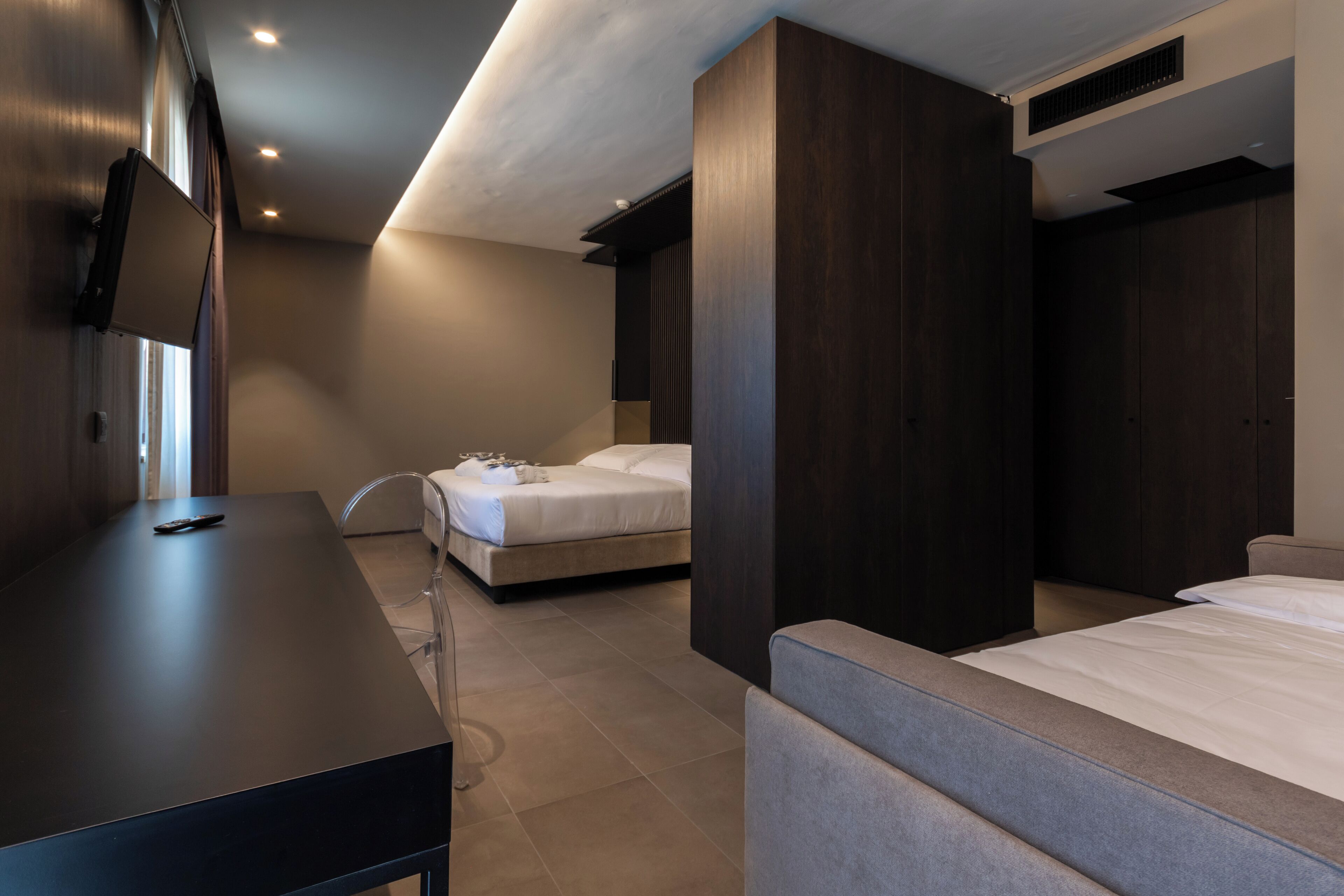 Ein modernes Hotelzimmer mit einem großen Bett, einem Einzelbett, einem Schreibtisch und einem an der Wand montierten Fernseher.