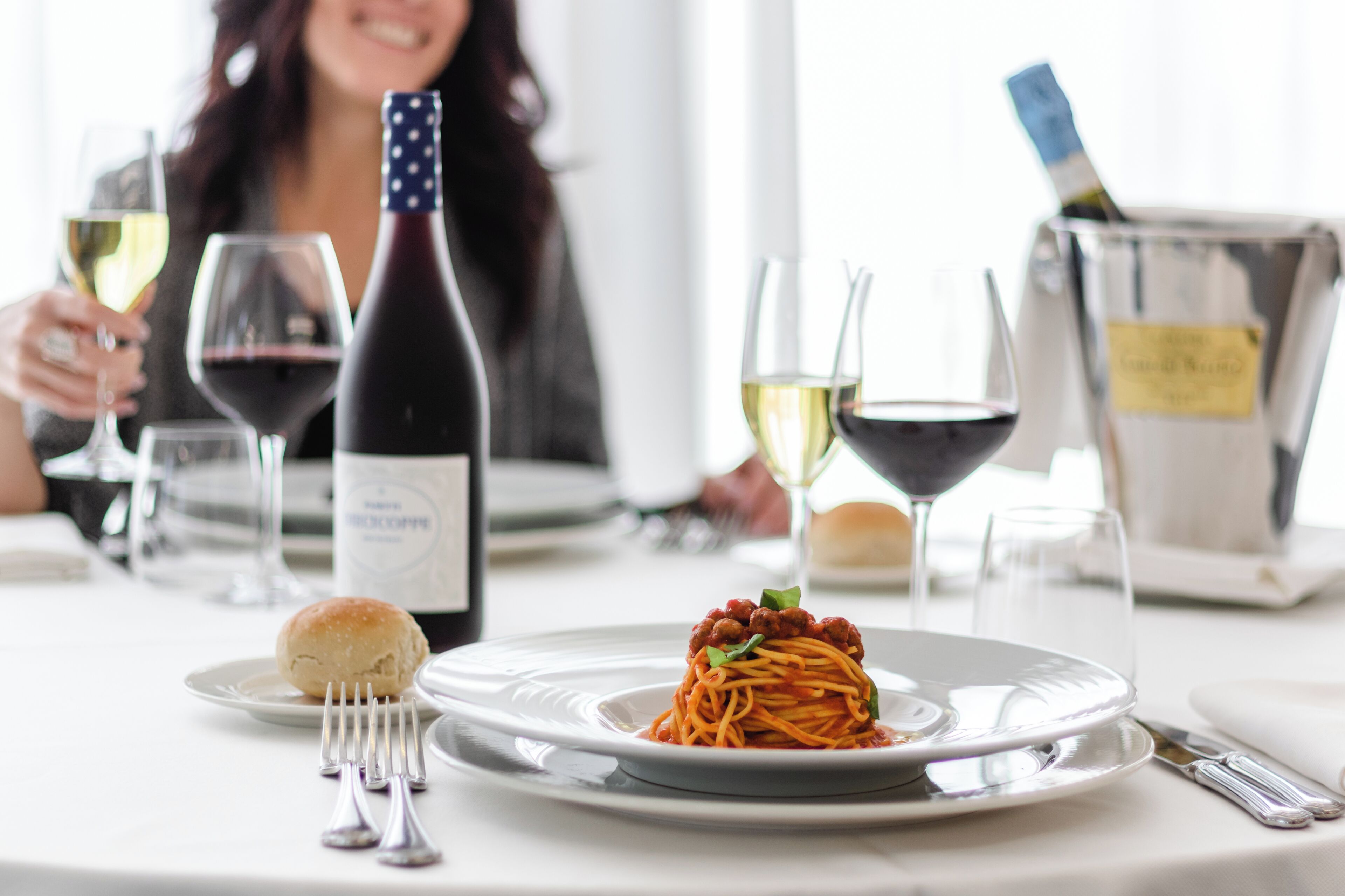 Una mesa de comedor con un plato de espagueti, copas de vino y una botella de vino.