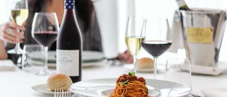 Una mesa de comedor con un plato de espagueti, copas de vino y una botella de vino.