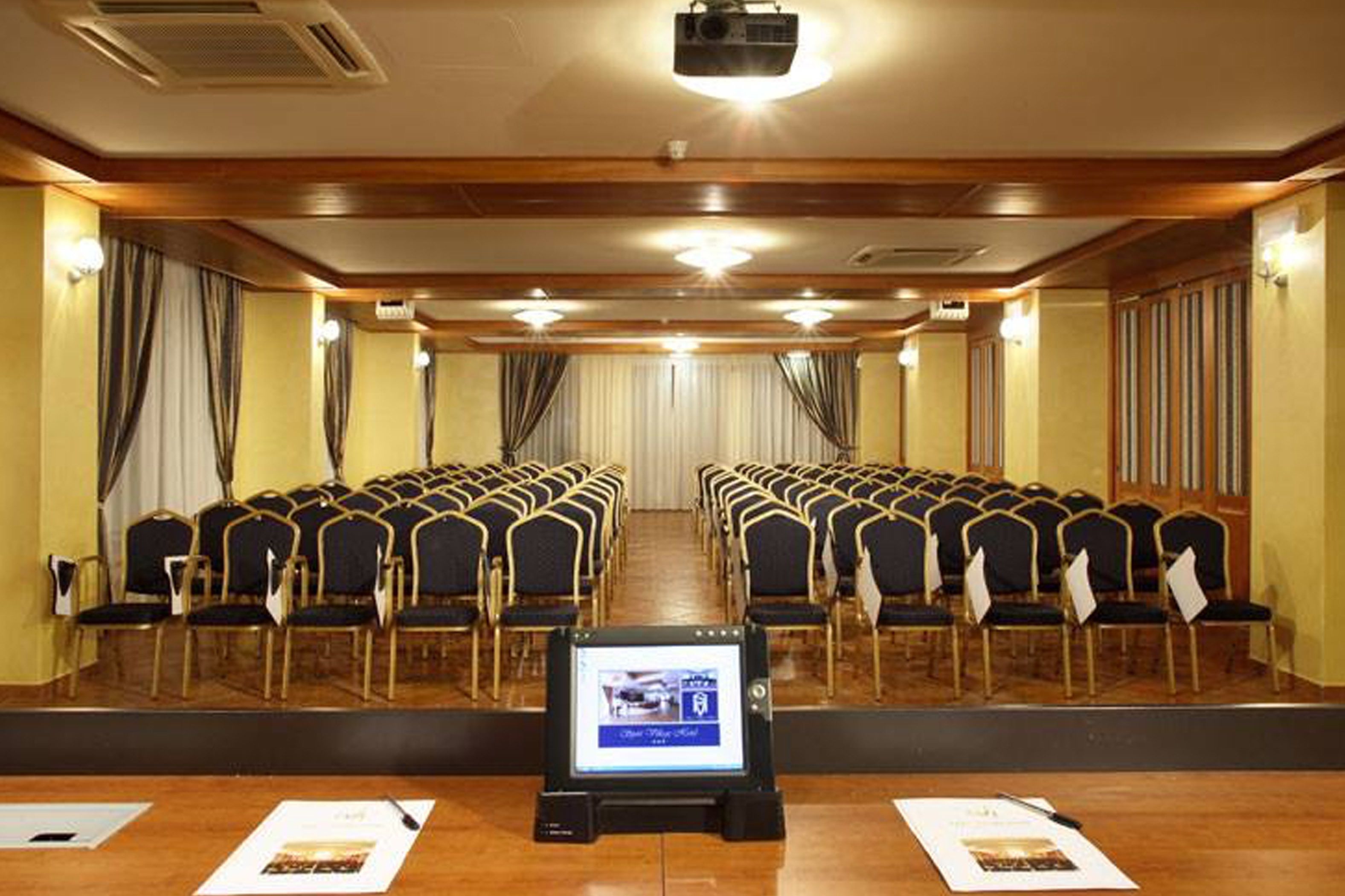 A conference room with rows of chairs, a podium, and a screen displaying an image.