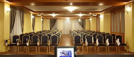 A conference room with rows of chairs, a podium, and a screen displaying an image.