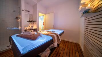 Un cuarto de spa con una camilla de masaje, zona de ducha y tocador con espejo.