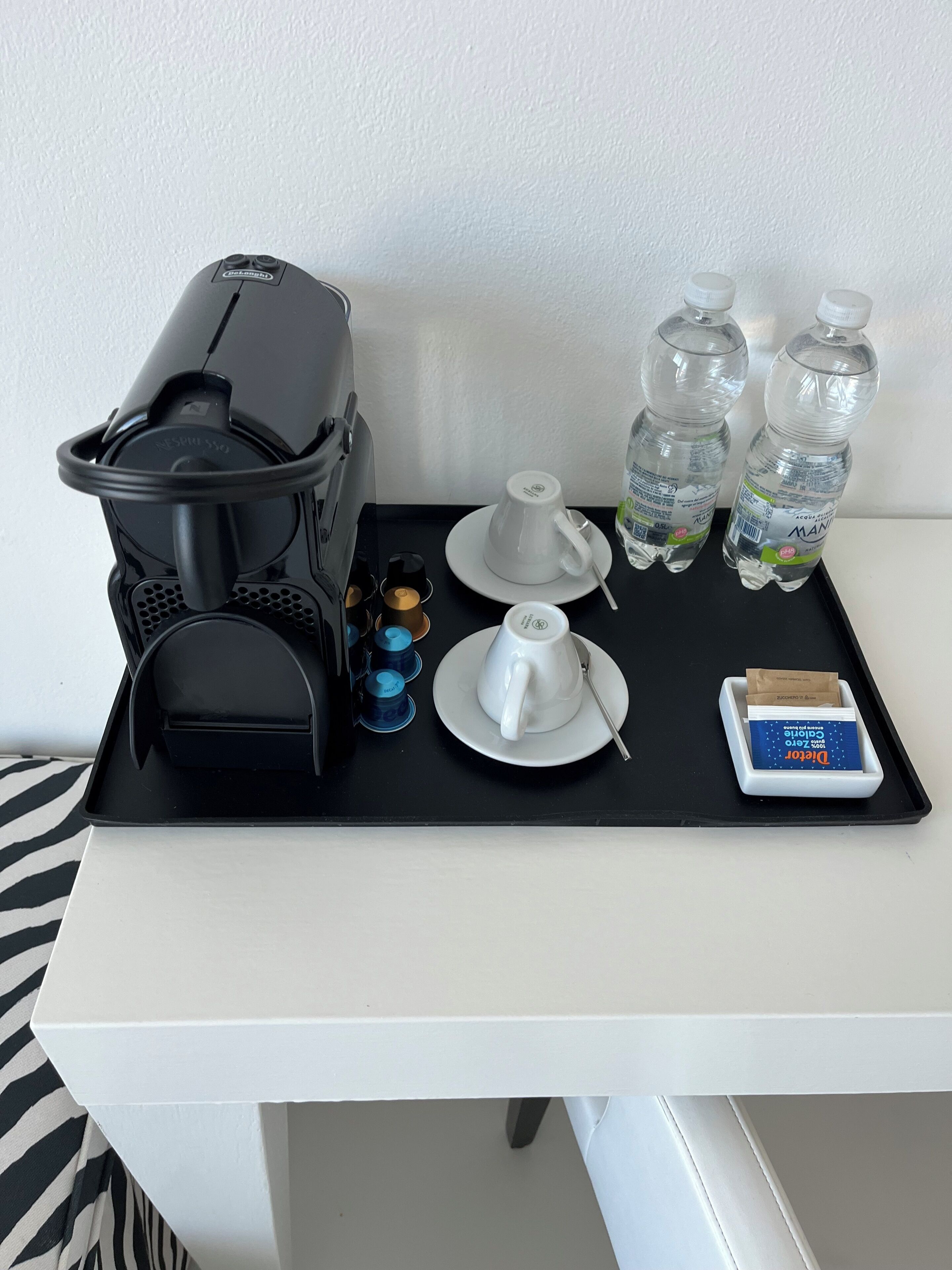 Een koffiezetapparaat, twee kopjes, twee waterflessen en een klein doosje op een dienblad.