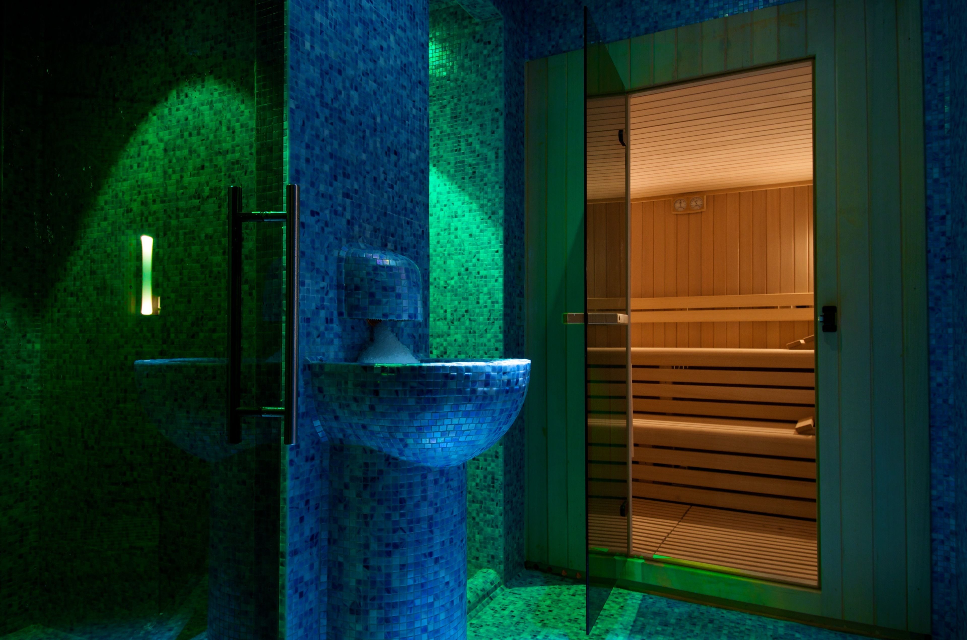 A bathroom with a mosaic sink, wooden sauna door, and a glass partition.