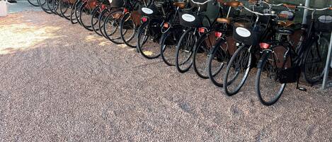 A row of bicycles under a green canopy, with a gravel ground.