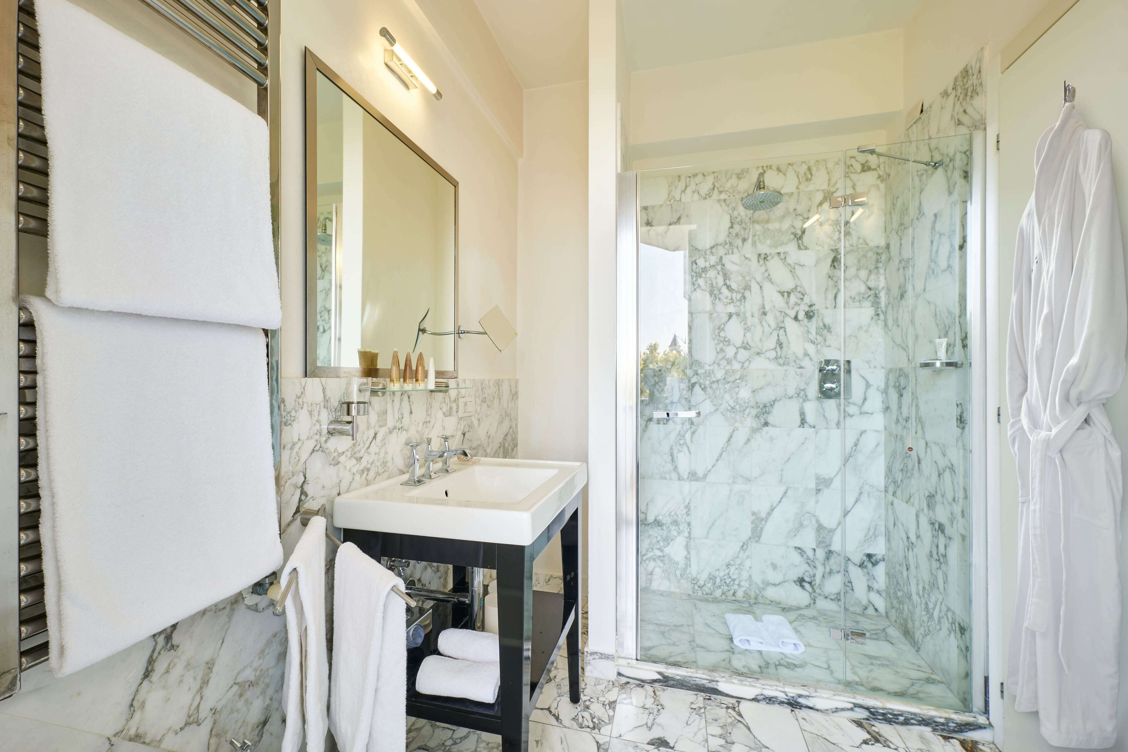 Un baño moderno con lavamanos de mármol, ducha con cerramiento de vidrio y un espejo grande.