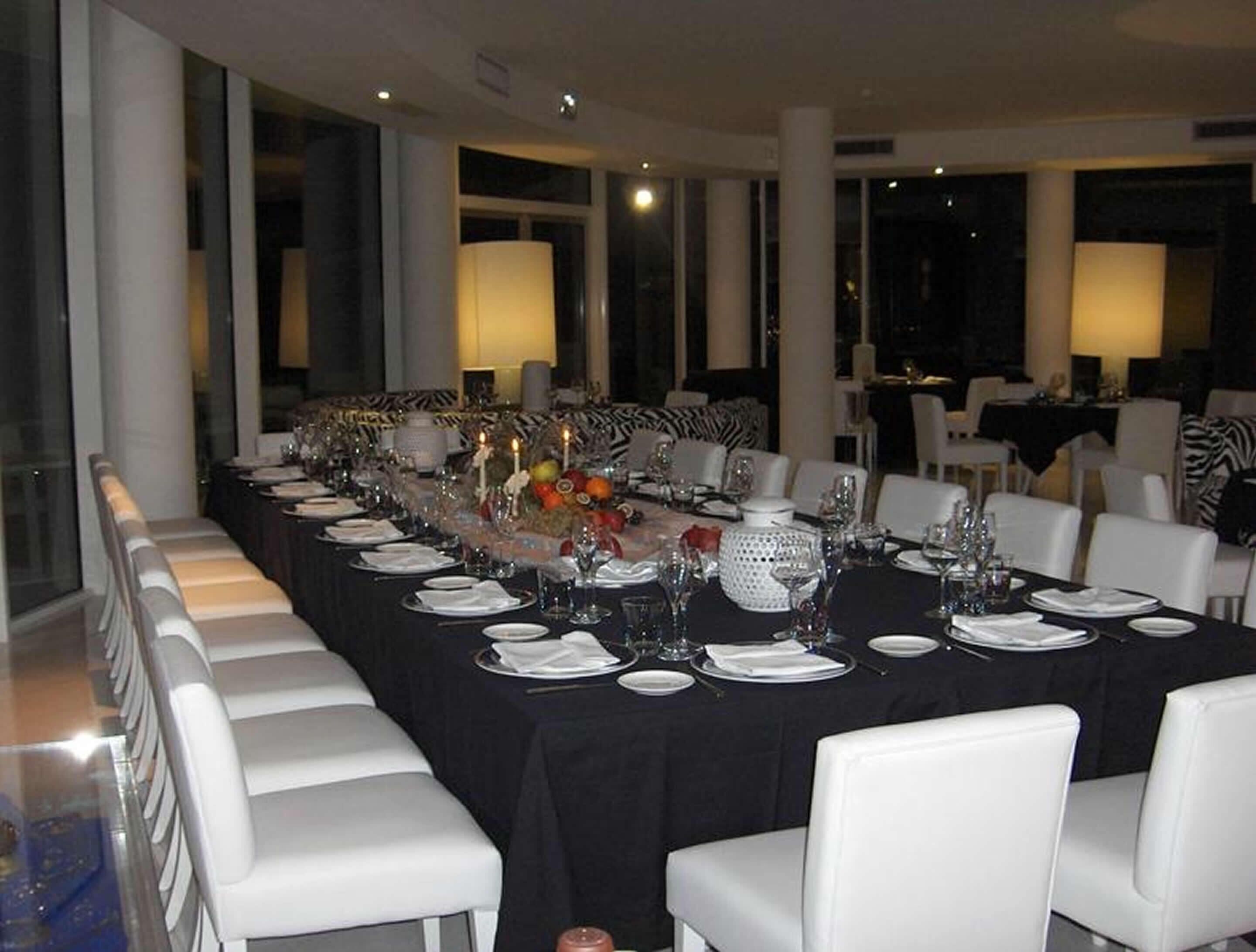 Une longue table à manger, agrémentée de chaises blanches, de bougies et d’un centre de table composé de fruits et de fleurs.