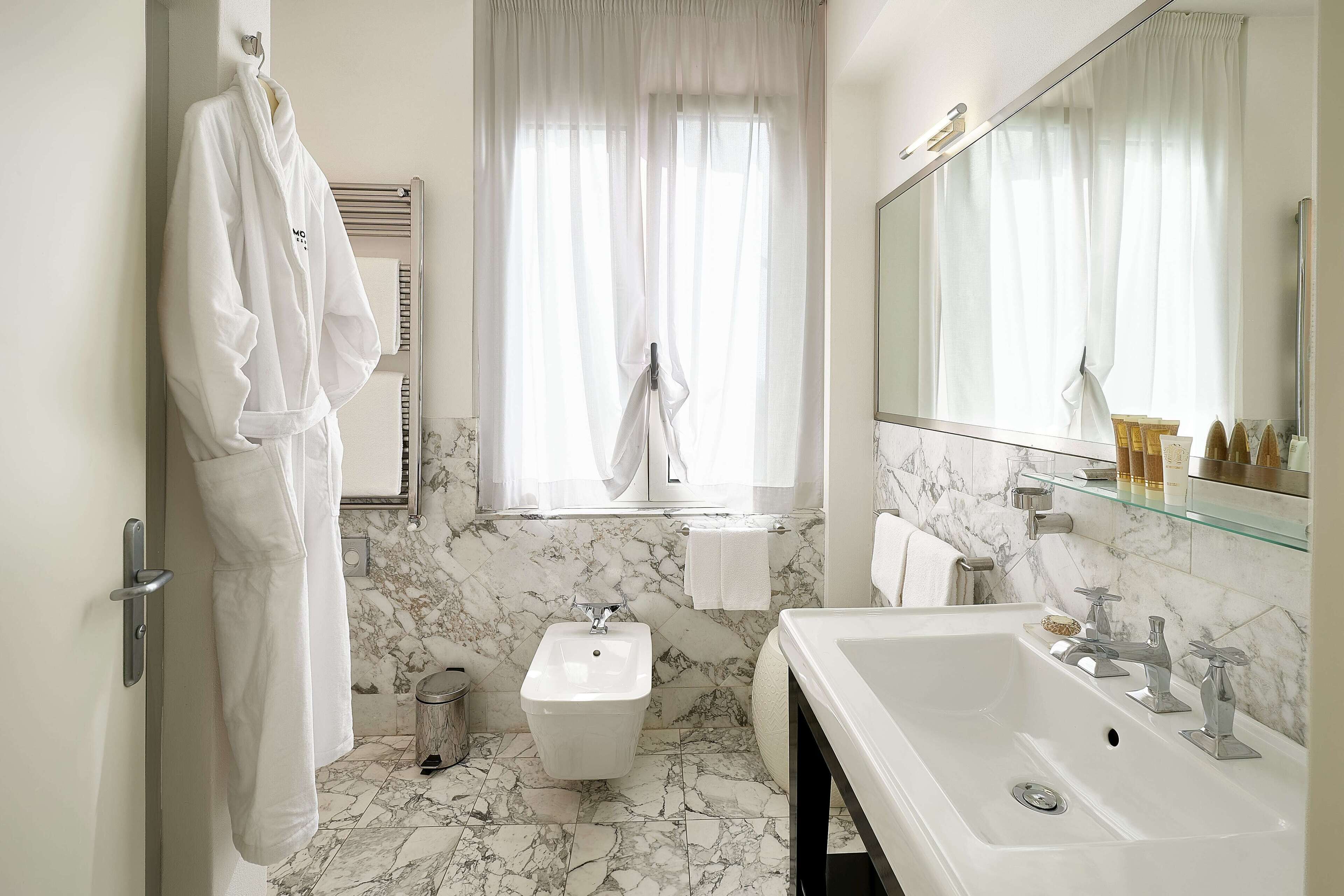 Un bagno moderno con pavimento in marmo, un lavandino capiente, un bidet e uno specchio con ripiano in vetro sopra.