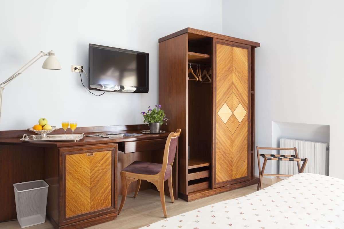 Une chambre d’hôtel avec un bureau en bois, une chaise, un téléviseur fixé au mur, une armoire et un radiateur.