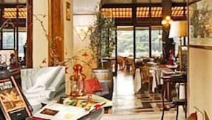 A cozy interior with a wooden bench, a table with a lamp, and a view through large windows. - Cacciani Hotel (Frascati)