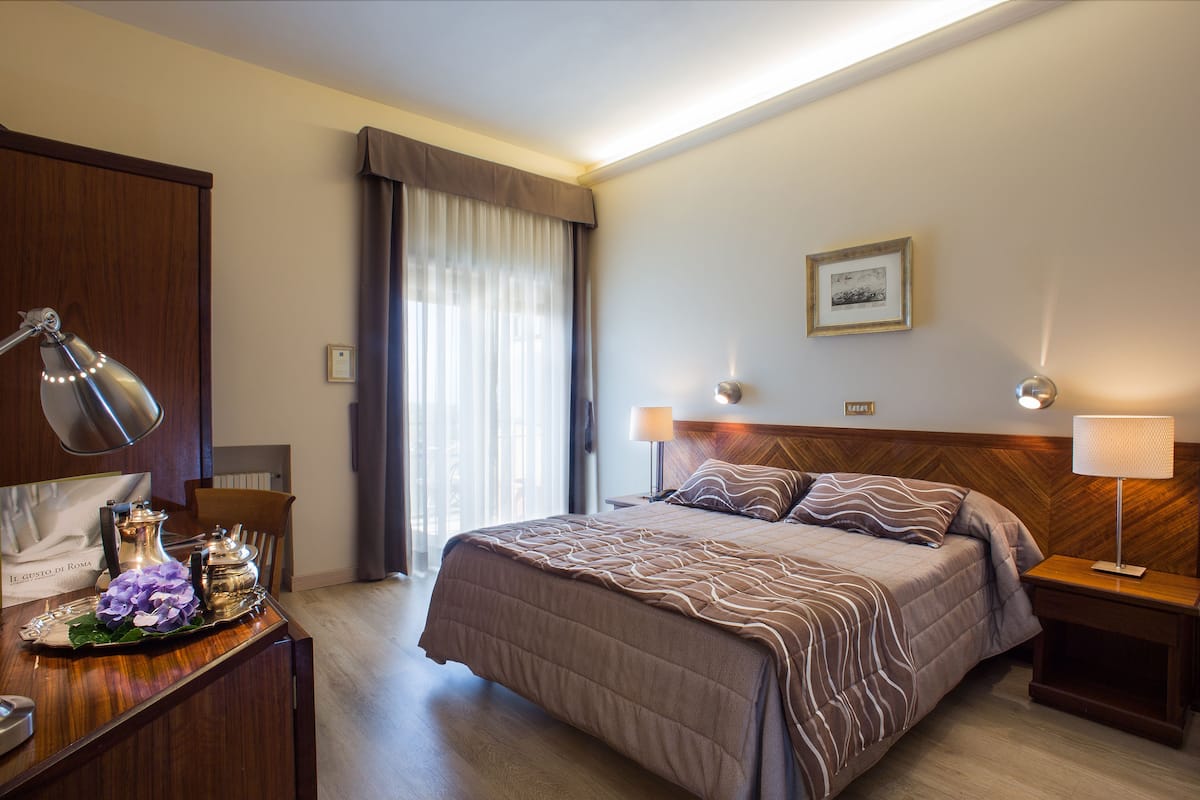 Une chambre d’hôtel avec un grand lit, des tables de chevet, un bureau avec une lampe et une fenêtre avec des rideaux.