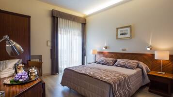 Una camera d'albergo con un letto grande, comodini, una scrivania con una lampada e una finestra con tende.