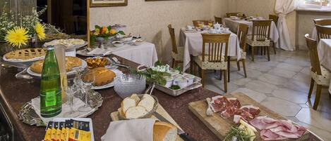 Un bufé de desayuno con diversas opciones de comida y una zona de cocina con tabla de cortar, cuchillo y hierbas aromáticas.