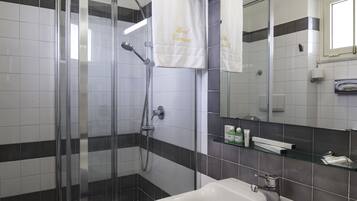 Un baño moderno con ducha envuelta en vidrio, un lavamanos blanco y un espejo grande.
