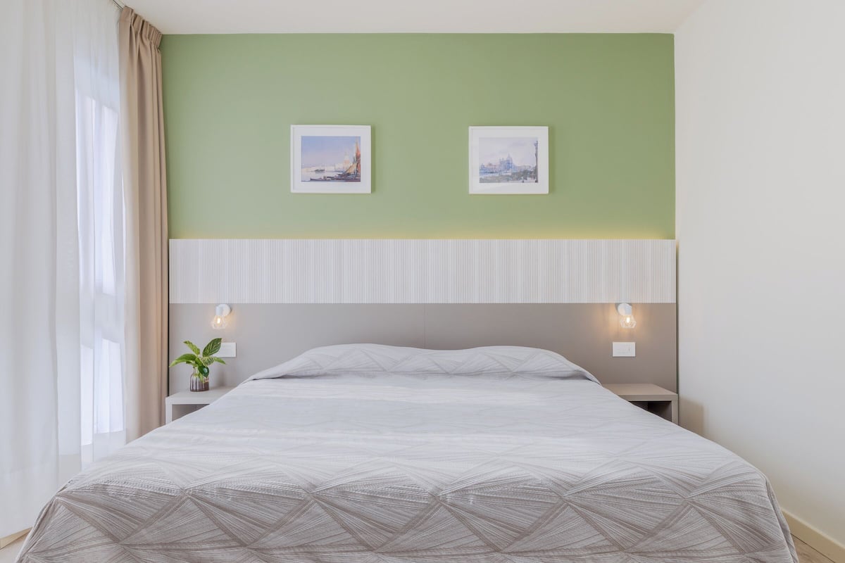 A bedroom with a bed, two wall-mounted pictures, a bedside table with a plant, and a nightstand with a lamp.