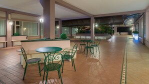 A spacious indoor area with multiple tables and chairs, a central seating area, and a view of a garden through large windows. - Hotel Palladio (Mestre)