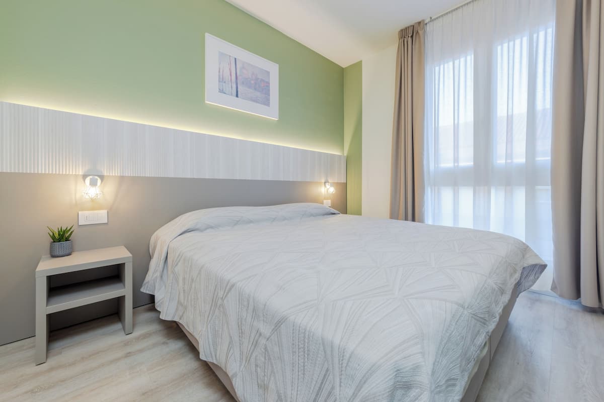 A modern bedroom with a bed, bedside tables, a wall-mounted light, and a window with curtains.