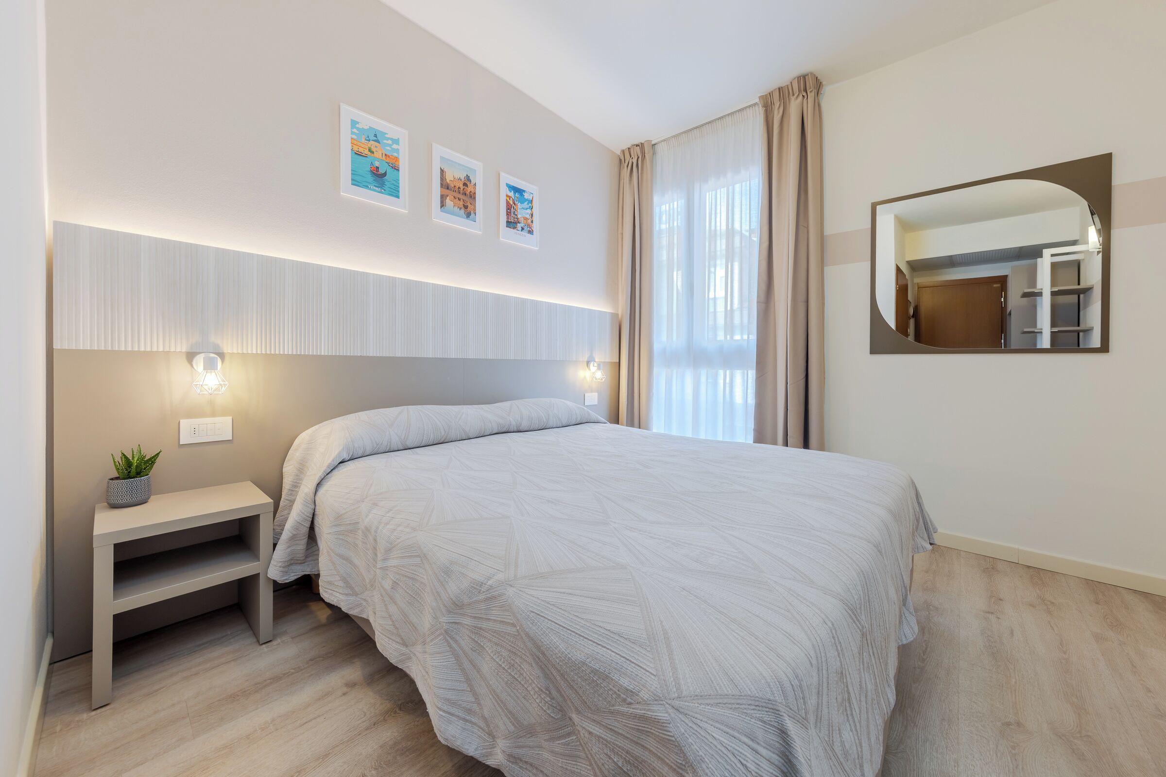 Un dormitorio con cama, mesita de noche, luz empotrada en la pared y un espejo.