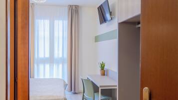 Ein Hotelzimmer mit Bett, Schreibtisch, Stuhl, Fernseher und Zimmerpflanze.