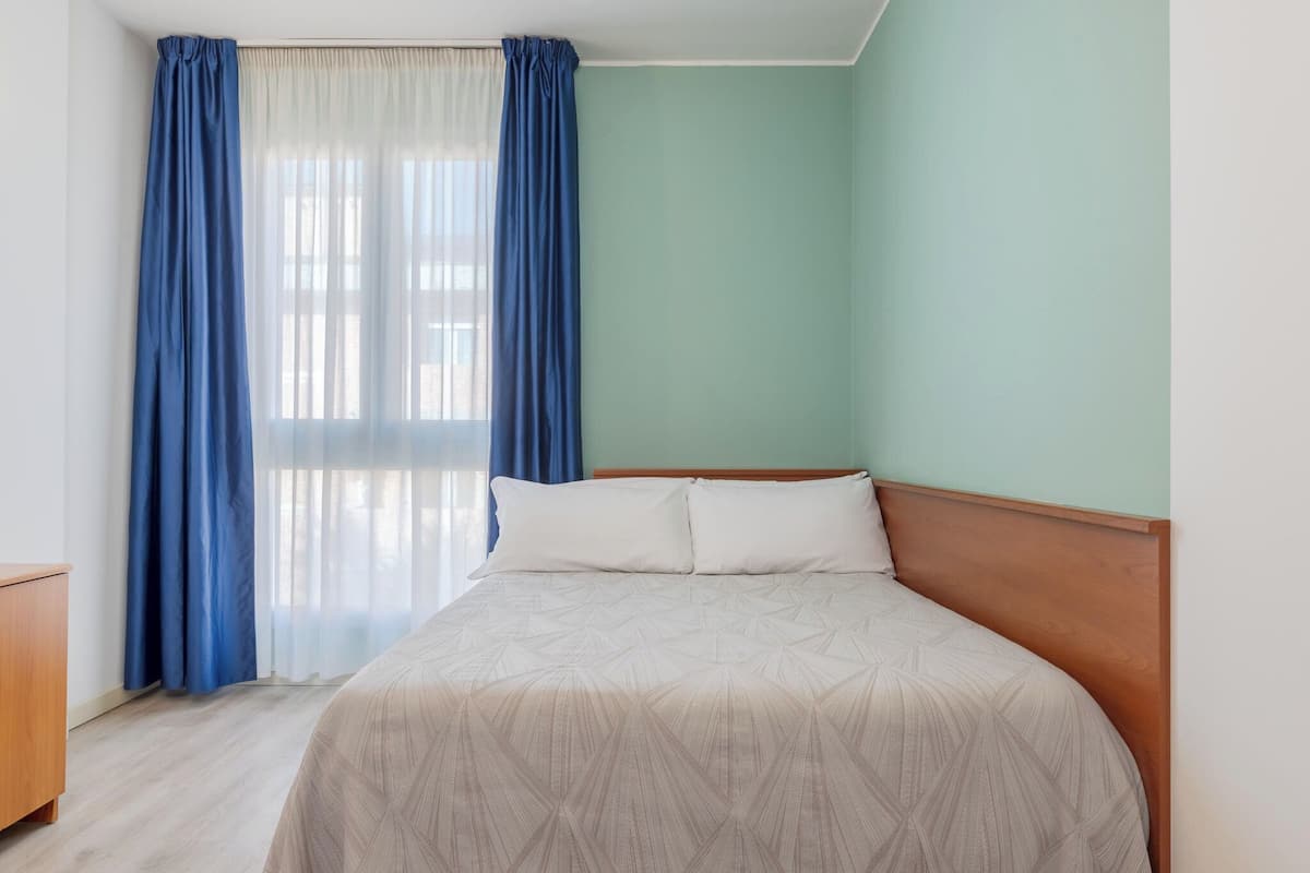A bedroom with a bed, a wooden headboard, and a window with blue curtains.
