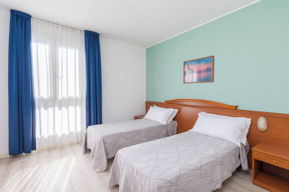 A hotel room with two beds, a wooden headboard, a nightstand, and a painting on the wall.