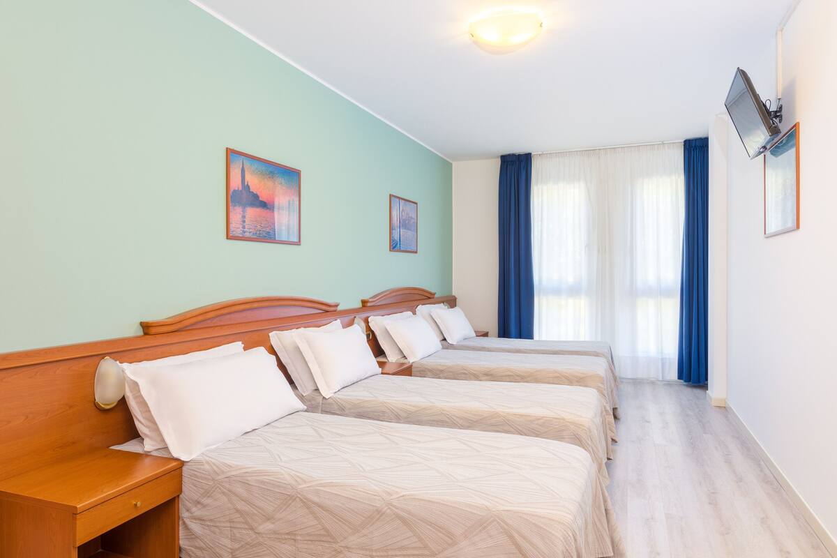 A hotel room with three beds, a wooden headboard, a nightstand, and a flat-screen TV mounted on the wall.