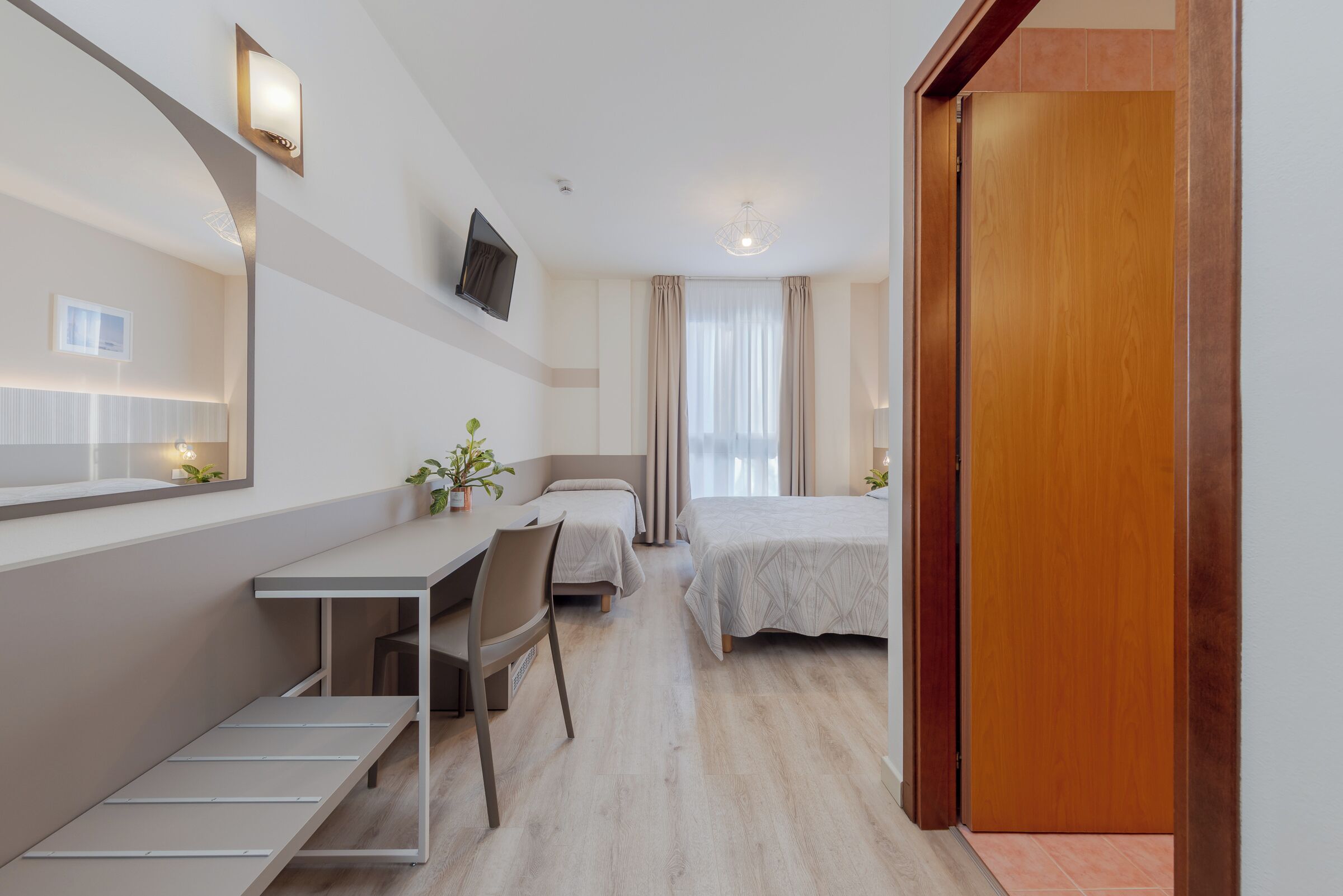 Habitación de hotel con escritorio, dos camas, televisor y puerta de madera.