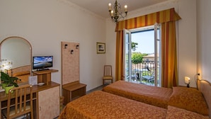 A hotel room with two beds, a television, a desk with a computer, a chair, a small table with a plant, and a balcony with outdoor furniture. - Hotel Villa Ombrosa (Pietrasanta)