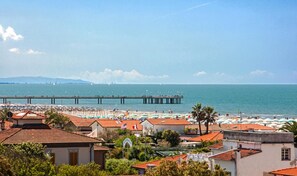 A coastal town with a pier extending into the sea, surrounded by beach umbrellas and a clear sky.