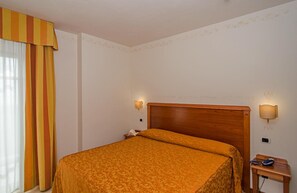 A hotel room with a wooden bed, two wall-mounted lamps, a nightstand, and a striped curtain.